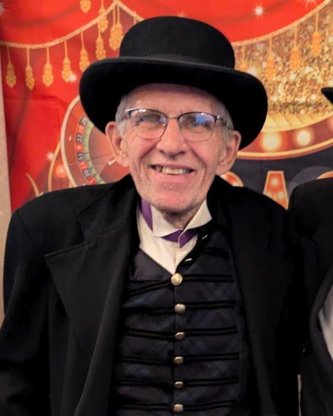 Norman Nelson smiling, wearing a bowler hat and glasses